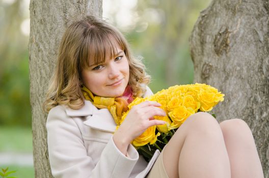 Young cute girl with a bouquet of yellow roses in autumn cool weather