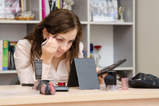 Young girl puts makeup in the office workplace