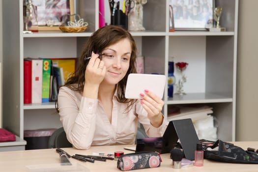 A young girl puts makeup in the office workplace