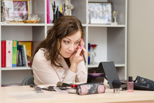 A young girl puts makeup in the office workplace