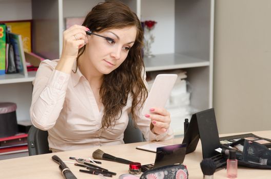 A young girl puts makeup in the office workplace