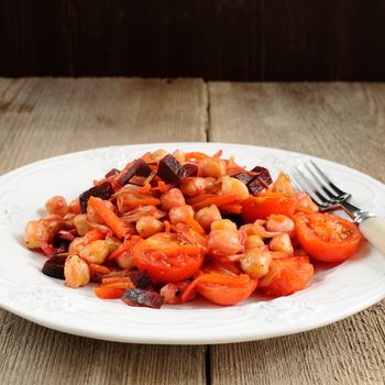 Red salad with chick peas, carrots chops, tomatoes and beetroots in white plate on wooden background