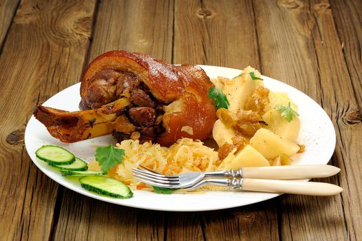 Eisbein in white plate with two forks on wooden background horizontal