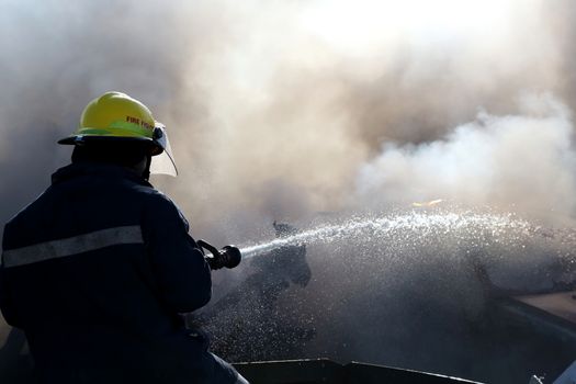 Fireman spraying water on a burnt out and smoking vehicle