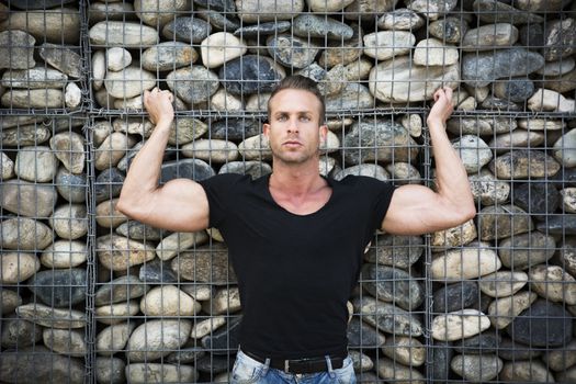 Muscular sexy man in front of stone wall, showing bulging biceps