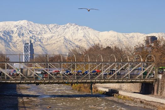 Snow covered mountains surrounding the city of Santiago, capital of Chile. View from a bridge across the Mapocho River in central Santiago.