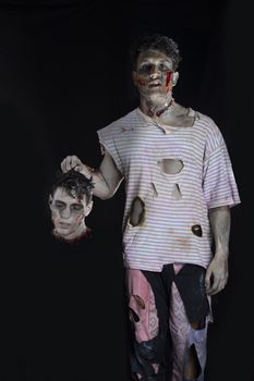 Scary creepy male zombie holding another man's head, isolated on black background