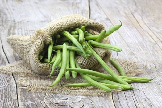 green beans in burlap sack on wooden background