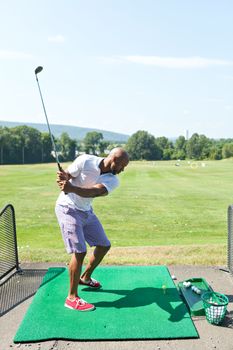Athletic golfer swinging at the driving range dressed in casual attire.