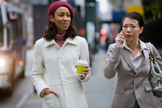 Two business women walking in the big city. One is on her cell phone.