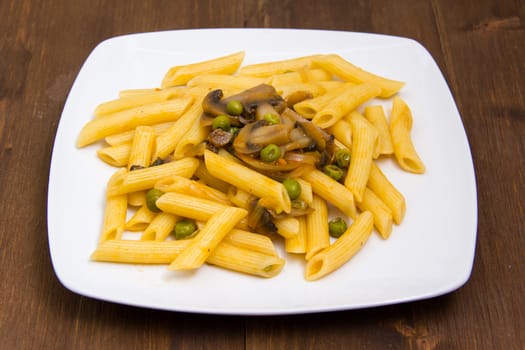 Pasta with mushrooms and peas on wooden table