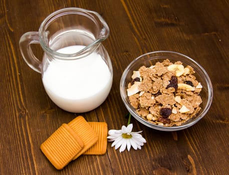 Jug of milk and cereal in bowl on wooden table seen from above