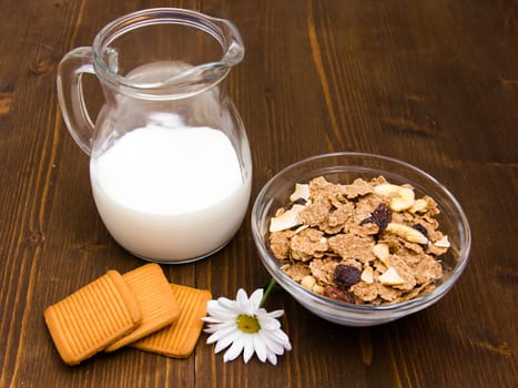 Jug of milk and cereal in bowl on wooden table