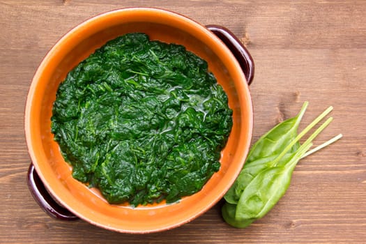 Spinach cooked in a pan on wooden table seen from above