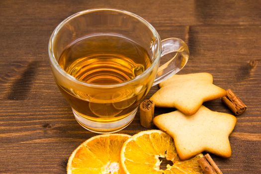 Tea and biscuits with orange and cinnamon on wooden table seen close
