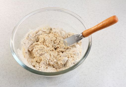 Mixing sticky raw multi seed malted bread mix with a palette knife in a glass bowl