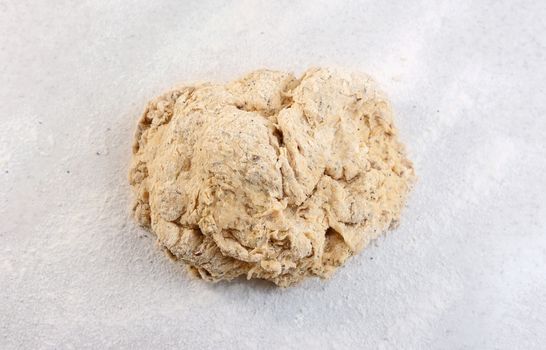 Rough ball of raw mixed seed bread dough on a floured worktop before kneading