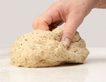 Close-up of a woman's hand kneading multi seed bread dough on a kitchen worktop