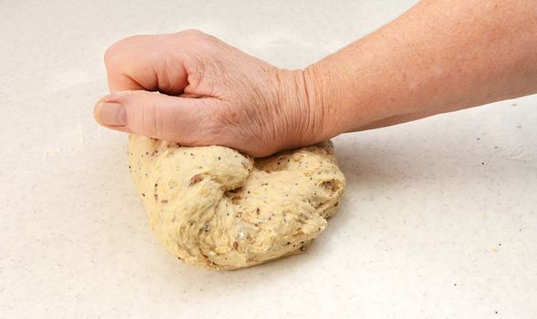 Woman's hand kneading multi seed malted bread dough on a floured work surface