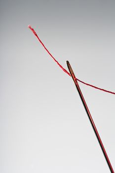 macro image of needle and red thread against grey background