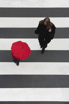 mother watching her child with red umbrella crossing the street