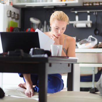 Female freelancer in her casual home clothing working remotly from her dining table in the morning. Home kitchen in the background.