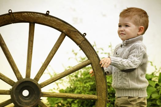 2 years old curious Baby boy with old wooden wheel 
