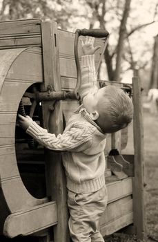 2 years old curious Baby boy managing with old agricultural Machinery on sepia brown color