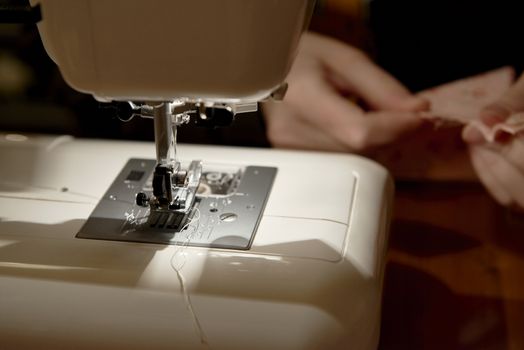 Detail of automatic sewing machine with hands working on piece of fabric in the background