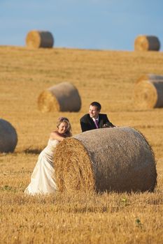 newly-wed couple in their wedding clothes in field of hay