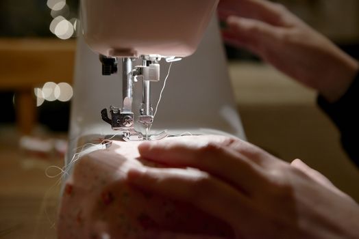 Detail of hands working on piece of fabric on automatic sewing machine, shot from the side