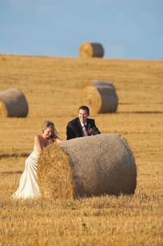 newly-wed couple in their wedding clothes in field of hay