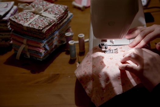 High angle detail of hands working on piece of fabric on automatic sewing machine, with fabric stacked on the side