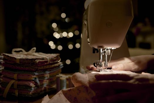 Low key detail of hands working on piece of fabric on automatic sewing machine, shot from the side