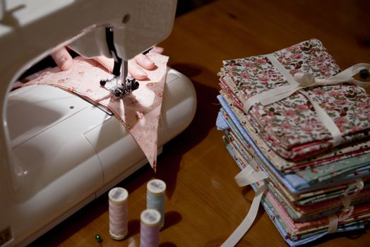 High angle detail of hands working on piece of fabric on automatic sewing machine, with fabric stacked on the side