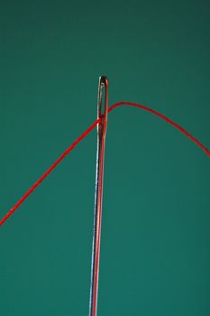 macro image of needle and red thread against colorful background