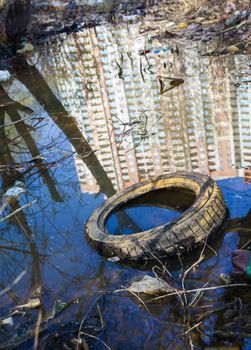 Garbage, old tire and reflection of the high-rise in the water on the landfill.