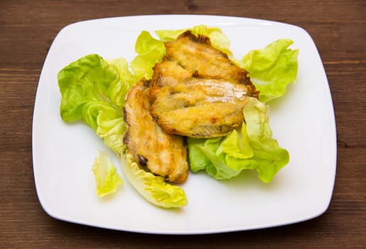 Fried fish on salad on wooden table