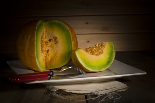 Sliced ripe spanspek, cantaloupe or sweet melon served on a platter on a table in front of a wooden wall with utensils for a healthy dessert