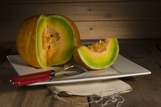 Sliced ripe spanspek, cantaloupe or sweet melon served on a platter on a table in front of a wooden wall with utensils for a healthy dessert