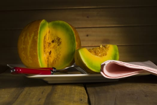 Sliced ripe spanspek, cantaloupe or sweet melon served on a platter on a table in front of a wooden wall with utensils for a healthy dessert