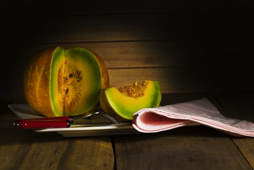 Sliced ripe spanspek, cantaloupe or sweet melon served on a platter on a table in front of a wooden wall with utensils for a healthy dessert