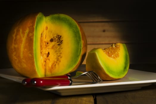 Sliced ripe spanspek, cantaloupe or sweet melon served on a platter on a table in front of a wooden wall with utensils for a healthy dessert