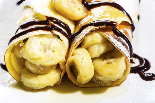 Delicious freshly baked pancakes or crepes filled with banana and drizzled with chocolate fort a gourmet dessert