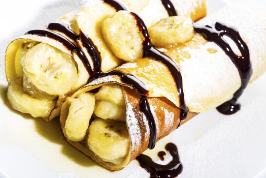 Delicious freshly baked pancakes or crepes filled with banana and drizzled with chocolate fort a gourmet dessert