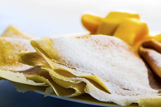 Freshly baked golden pancakes  or crepes neatly folded in a plate and served with fresh diced tropical fruit, close up view