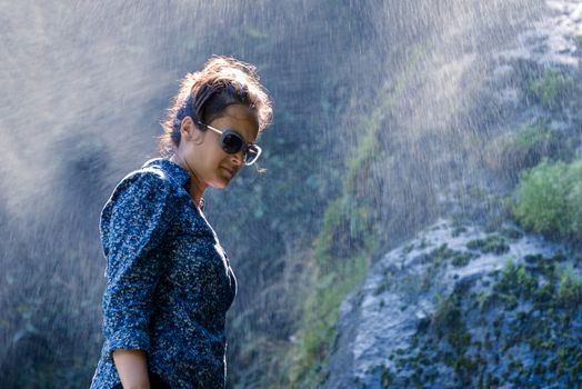 Young Nepalese woman standing in the water spray from a waterfall