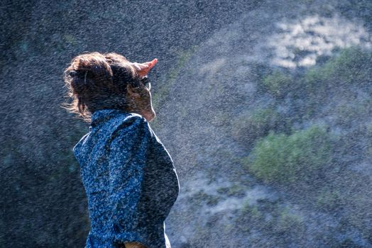 Young Nepalese woman standing in the water spray from a waterfall