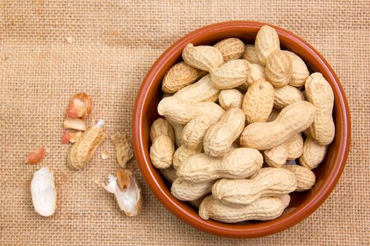 Peanuts in rustic bowl on jute mat seen from above