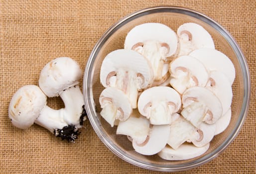 Sliced mushrooms in bowl on placemat jute seen from above